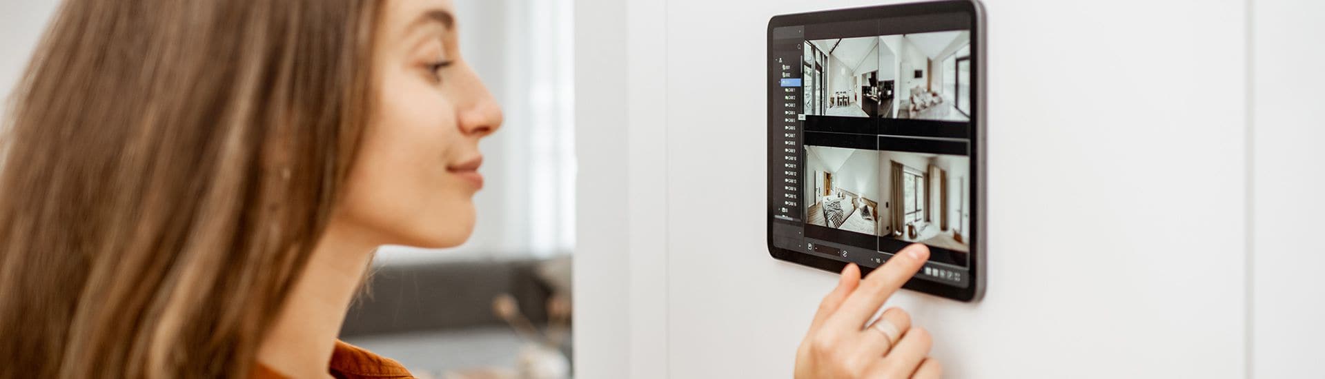 Frau bedient ein Wand-Tablet das KNX Smart Home System mit Überwachungskamera-Ansicht.