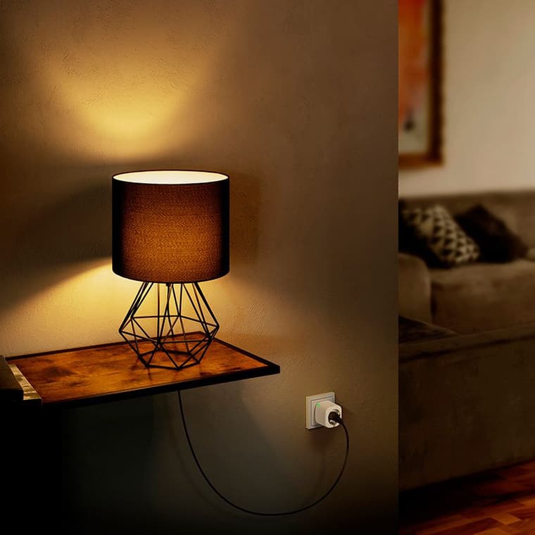 Tischlampe mit schwarzem Lampenschirm und geometrischem Metallfuß leuchtet auf Holztisch, Stecker in Steckdose.