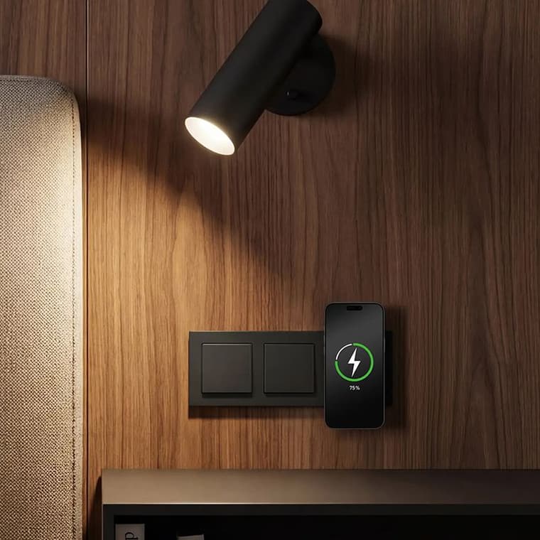 Holzvertäfelte Wand mit Leselampe, schwarzen Schaltern und einem Smartphone, das kabellos an der Wand lädt.