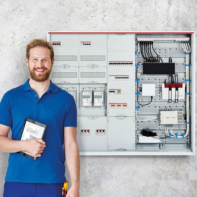 Elektriker mit Tablet steht vor einem geöffneten ComfortLine Zählerschrank mit Zählern, Sicherungen und sauber verlegter Verkabelung.