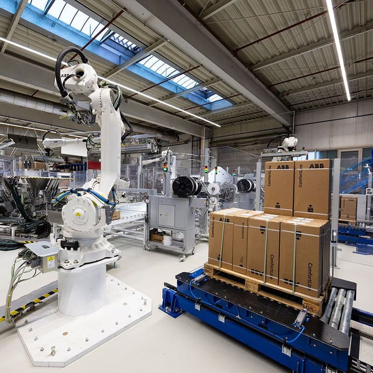 Industrieroboter von ABB stapelt Kartons mit der Aufschrift „ComfortLine“ auf einer Palette in einer modernen Fabrikhalle.